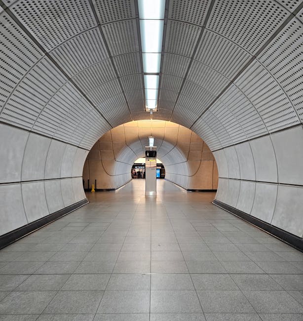 A spacious corridor near Edgware Tube Station with polished, light grey granite flooring reflecting overhead lighting, which enhances the clean appearance of the surface. The area features modern, whi